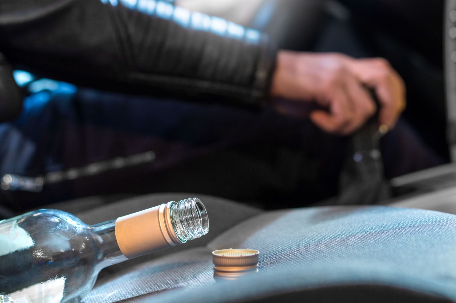 Young man driving car under the influence of alcohol. Hand on gear stick. Close up of empty bottle of wine on front seat. Traffic safety risk.